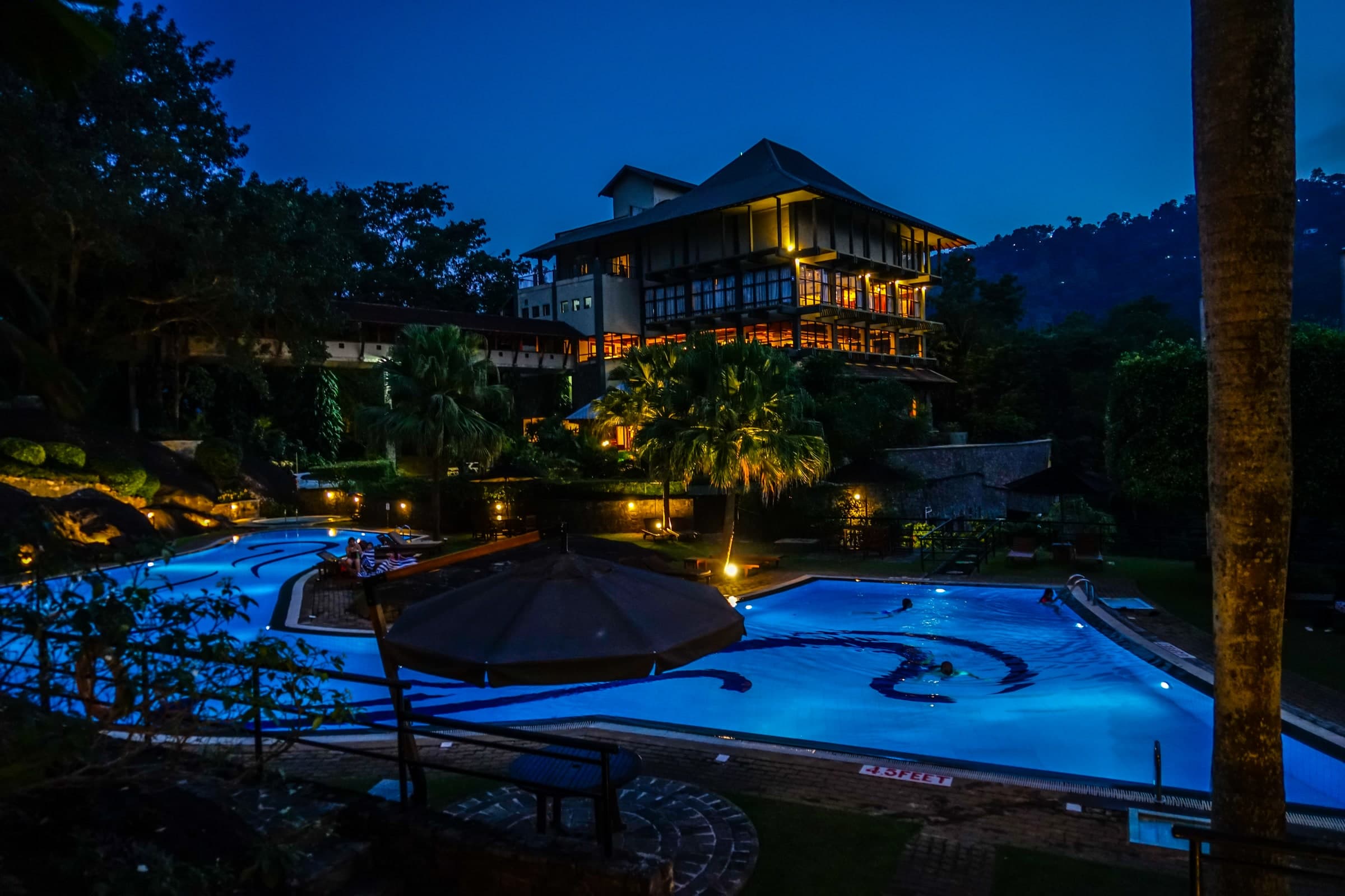 Hotel and swimming pool illuminated at dusk in Kandy