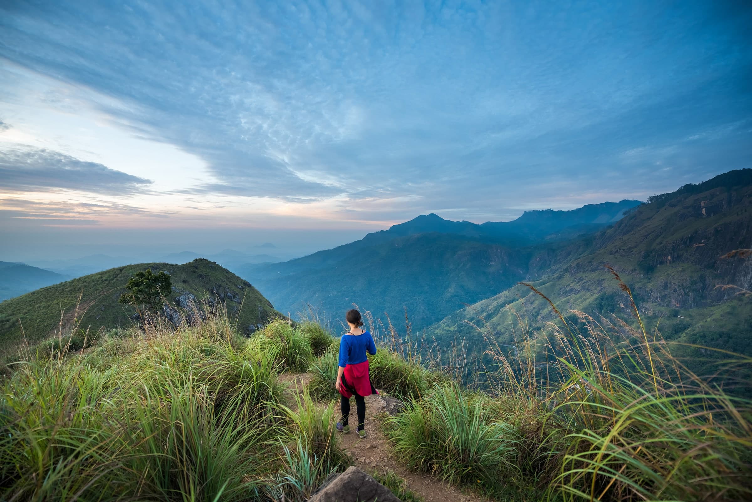 Hiker on a grassy ridge above the mountains near Ella